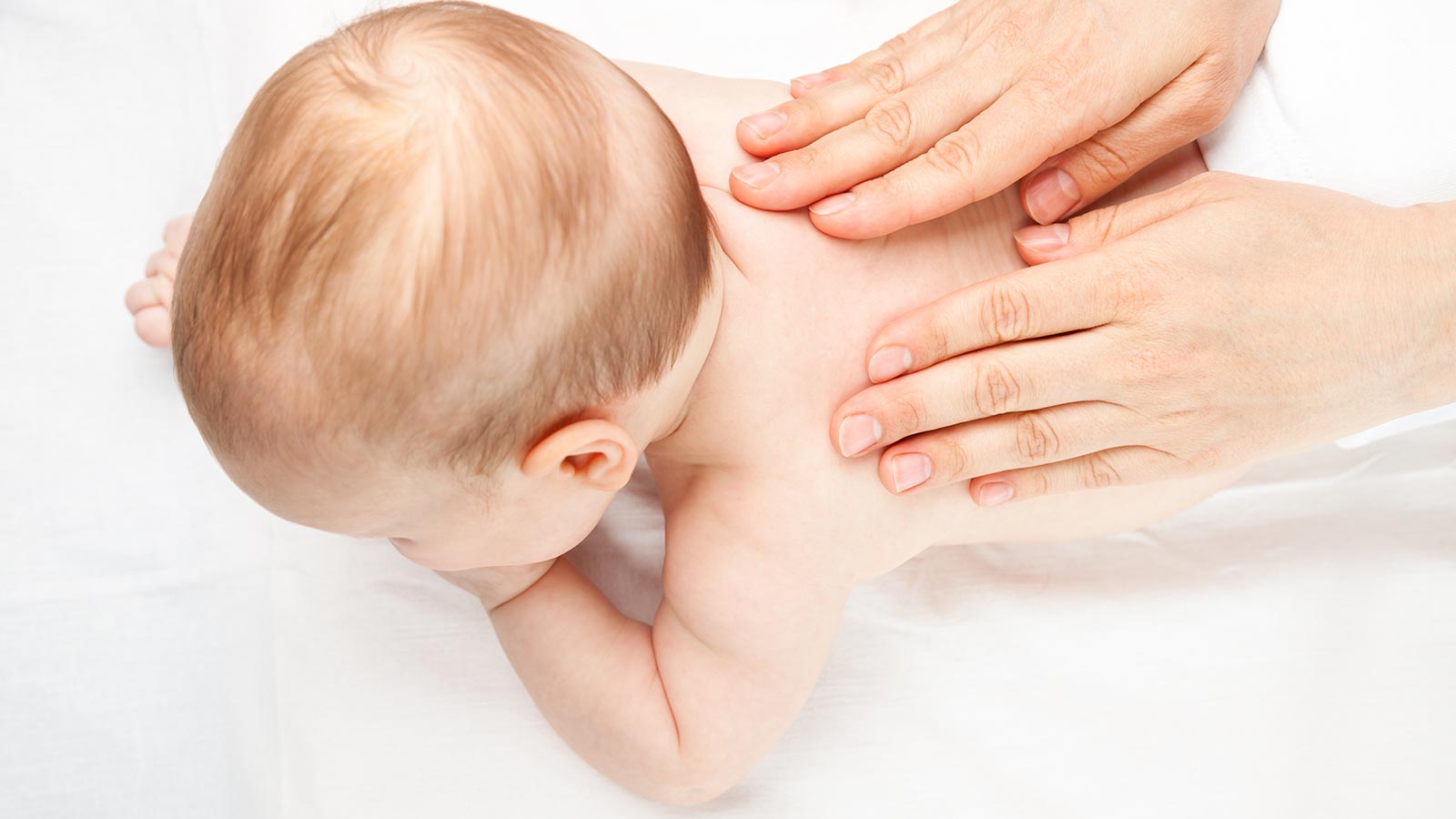 Foto eines Babys in Bauchlage, bei dem die Wirbelsäule abgetastet wird