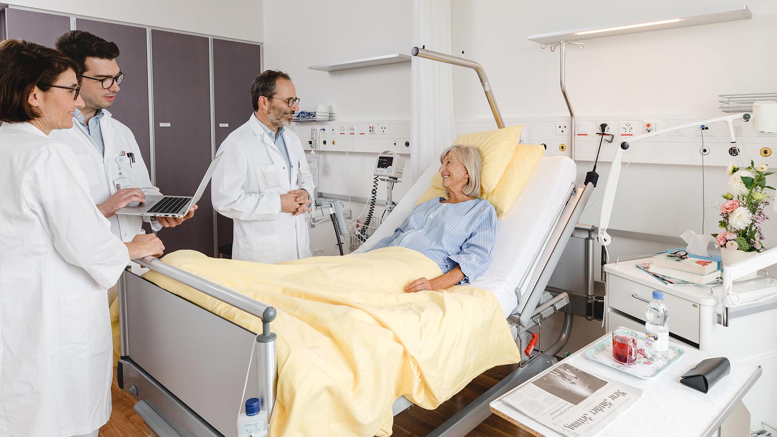 Zwei Ärzte und eine Pflegefachpersonen stehen am Bett einer Patientin